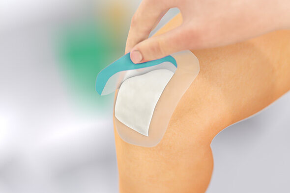 Person fjerner beskyttelsesfilmen fra Sorbact Secure-bandagen på knæet.